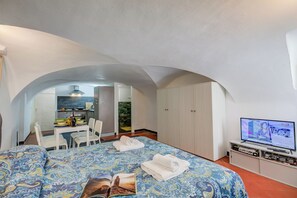 A hotel room with a bed, a TV, a dining area, and a kitchen in the background.