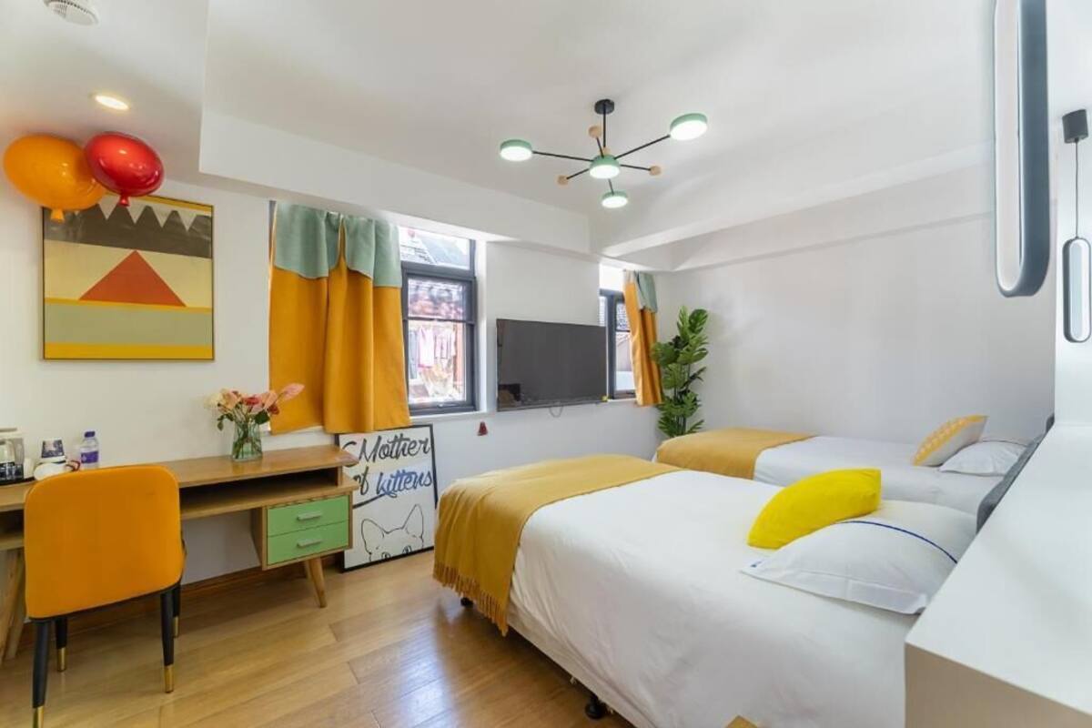 Un dormitorio con cama, escritorio y silla. Se ve una ventana con cortinas, una planta y un cartel en la pared.