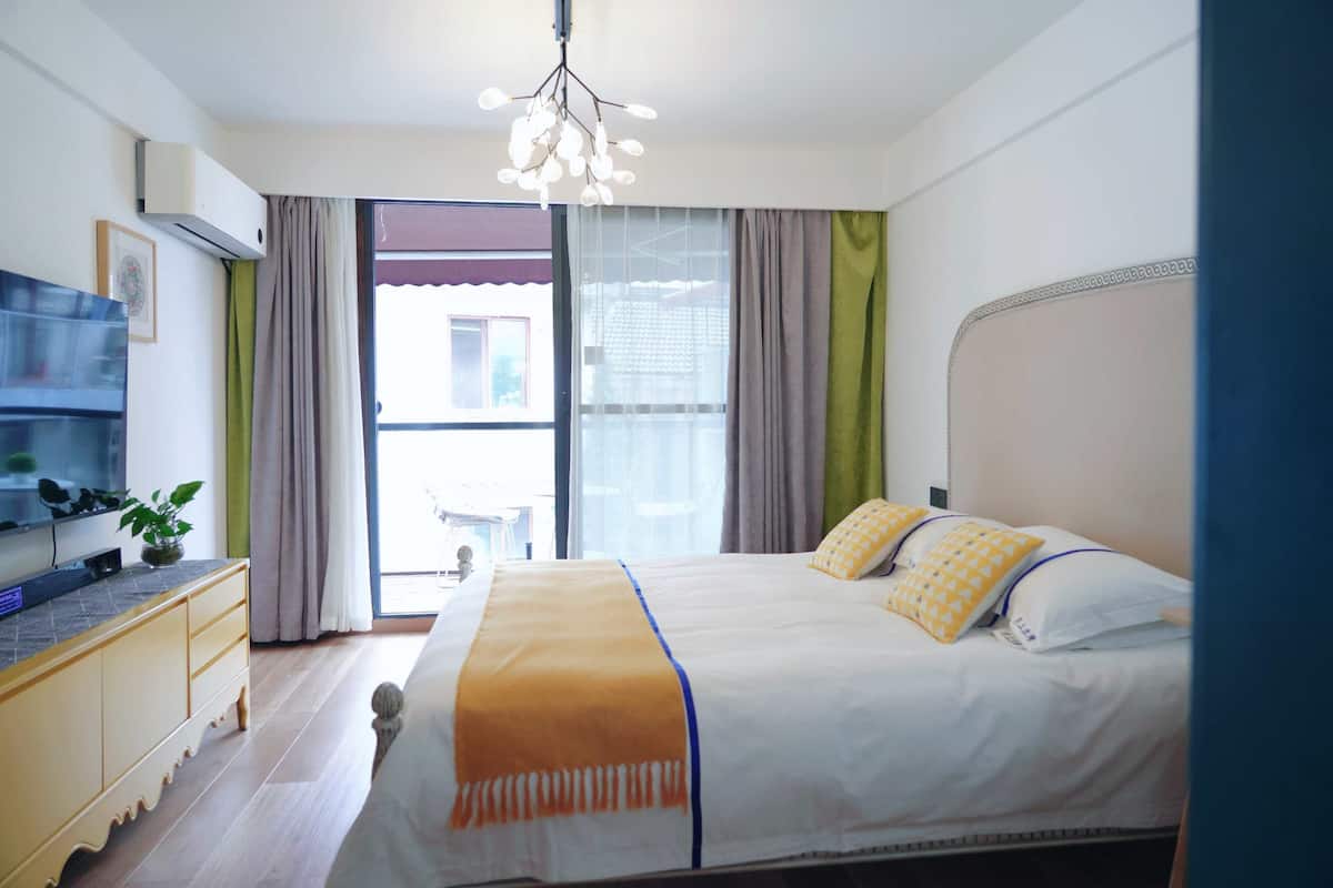 Un dormitorio con cama, cómoda, planta y ventana con cortinas.