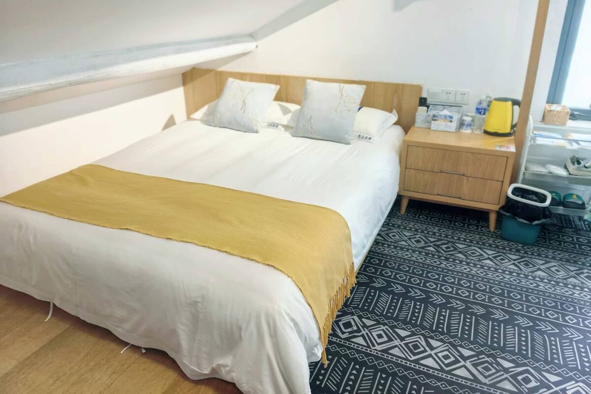 Una cama bien tendida con una colcha blanca y dorada, una mesita de noche de madera con una lámpara y un suelo con diseño.