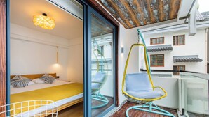 Quarto com cama, cadeira suspensa e varanda com vista para edifícios.