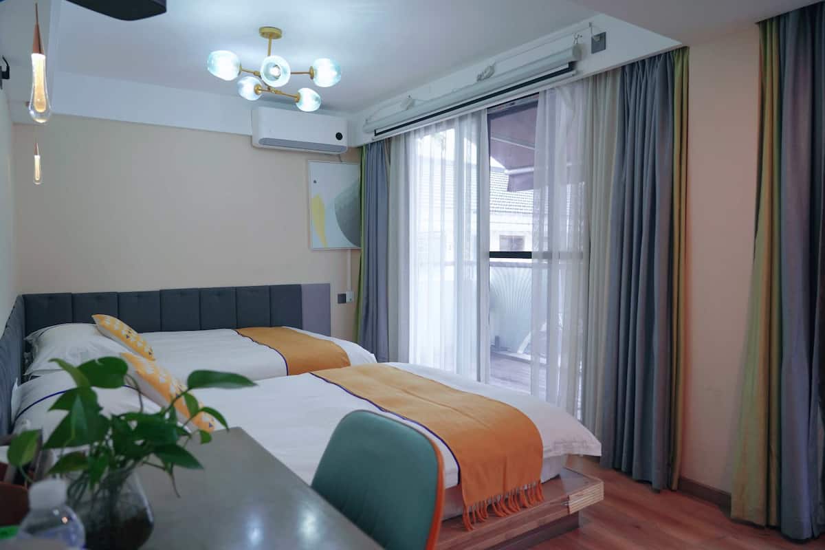 Una habitación de hotel con cama, escritorio, silla, planta y ventana con cortinas.