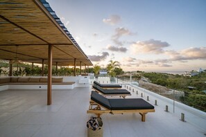 Eine Dachterrasse mit Liegestühlen, einer überdachten Sitzecke und Blick auf Meer und Grünflächen.