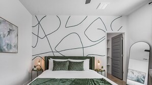 Quarto moderno com cama grande, arte abstrata na parede e manta verde.