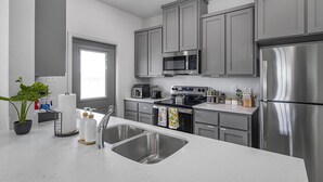 Uma cozinha moderna com eletrodomésticos de aço inoxidável, armários cinza e bancada branca.