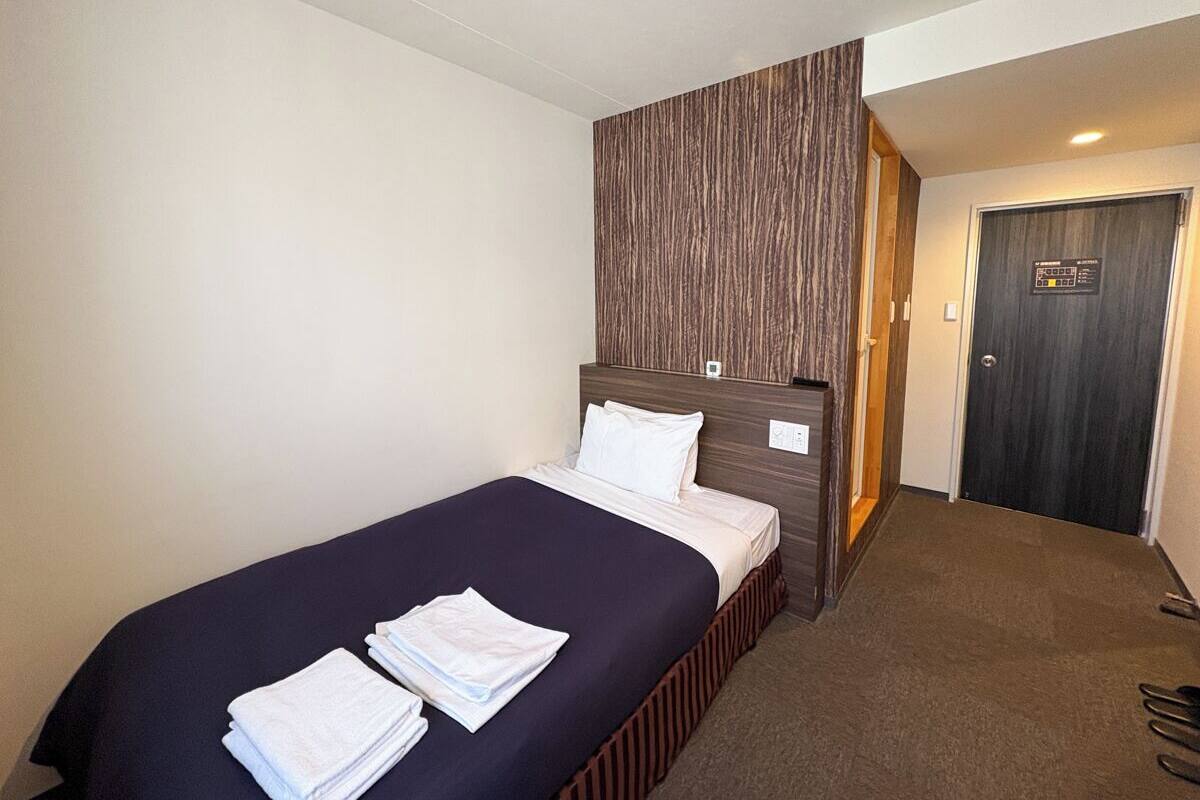 Habitación de hotel con una cama, cabecera de madera, una puerta y suelo alfombrado.