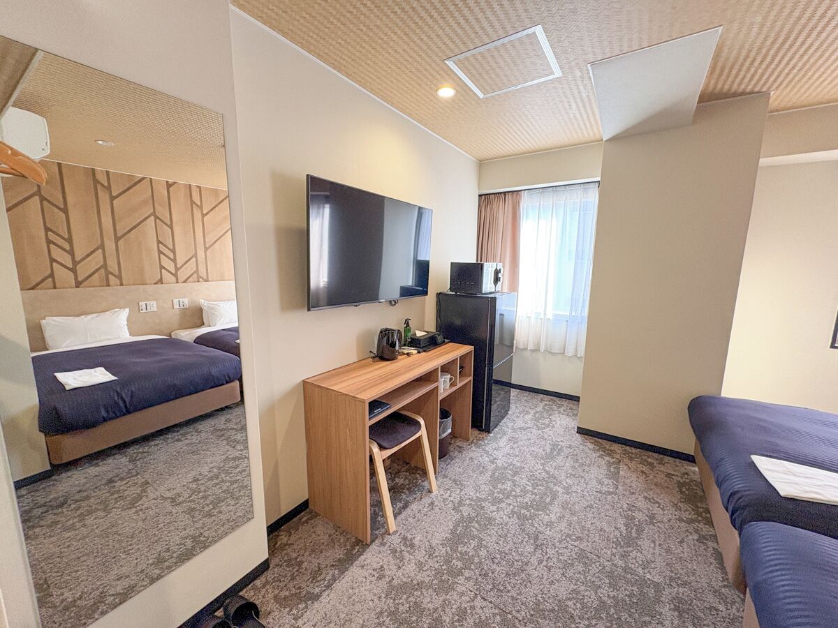 A compact hotel room with a bed, a desk with a chair, a television, and a refrigerator.