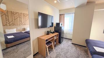 A compact hotel room with a bed, a desk with a chair, a television, and a refrigerator.
