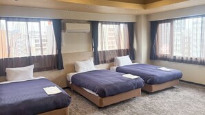 Habitació d'hotel amb tres llits, un sofà i una finestra gran amb cortines.