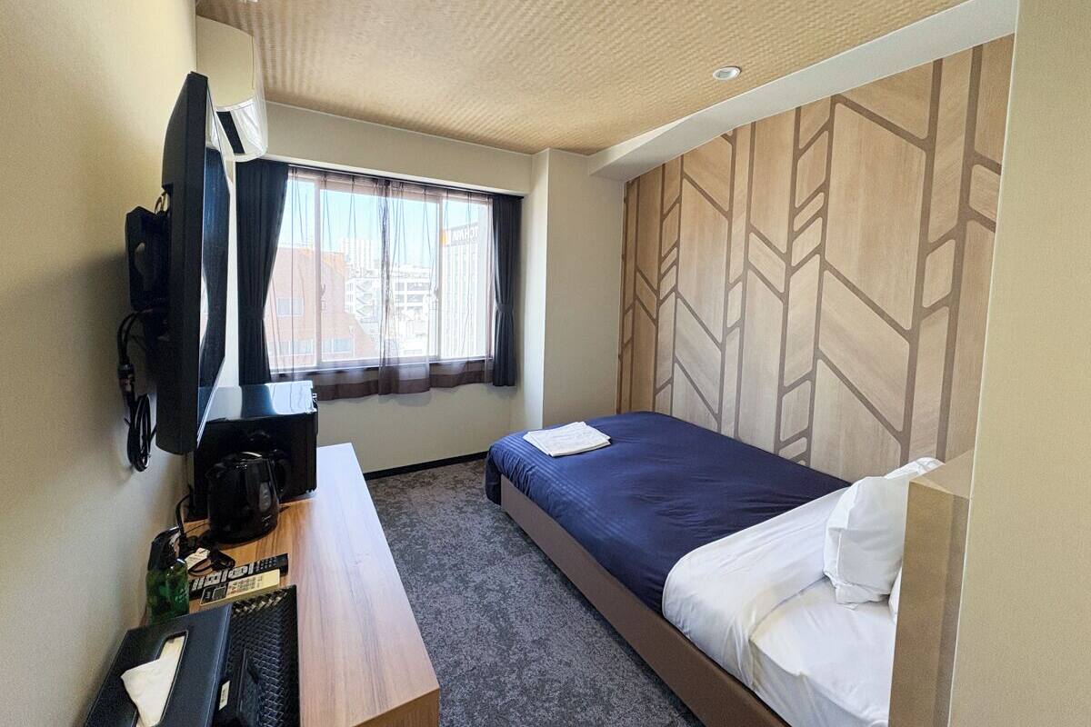 Una habitación de hotel con cama, escritorio con cafetera, televisión y ventana con cortinas.