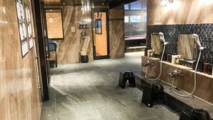 Un bany modern amb parets de marbre, zona de dutxa amb vària aixetes i un petit tamboret.