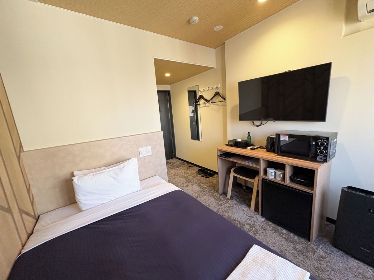 A hotel room with a bed, a desk with a microwave, a TV, and a small refrigerator.
