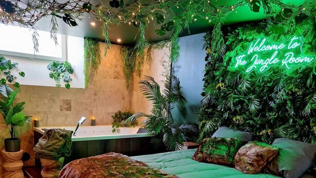 A bedroom with a green-themed jungle design, including a bed, pillows, and hanging plants. - Tropical escape Suite Jungle Room (Thiers)