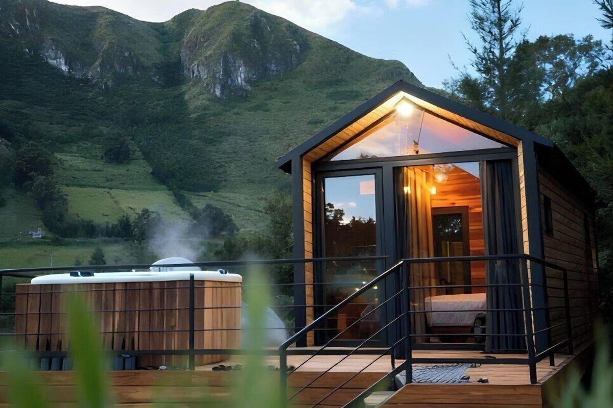 A wooden cabin with a glass entrance, a hot tub, and a bed.