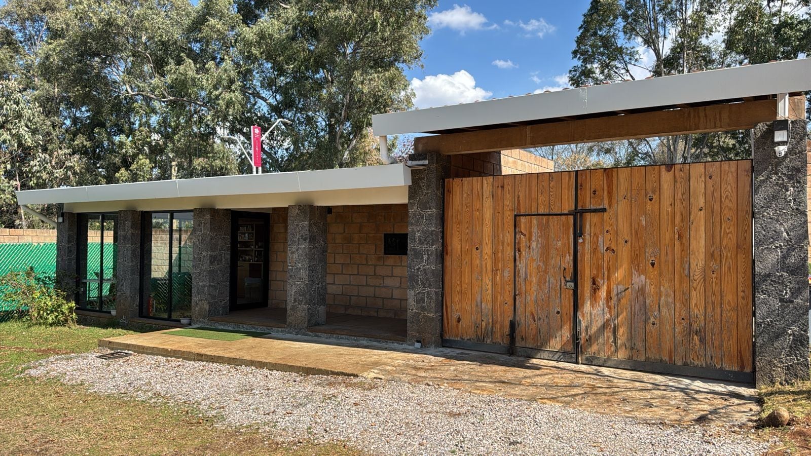 Un edificio moderno con un amplio portón de madera, pilares de piedra y una zona de entrada cubierta.