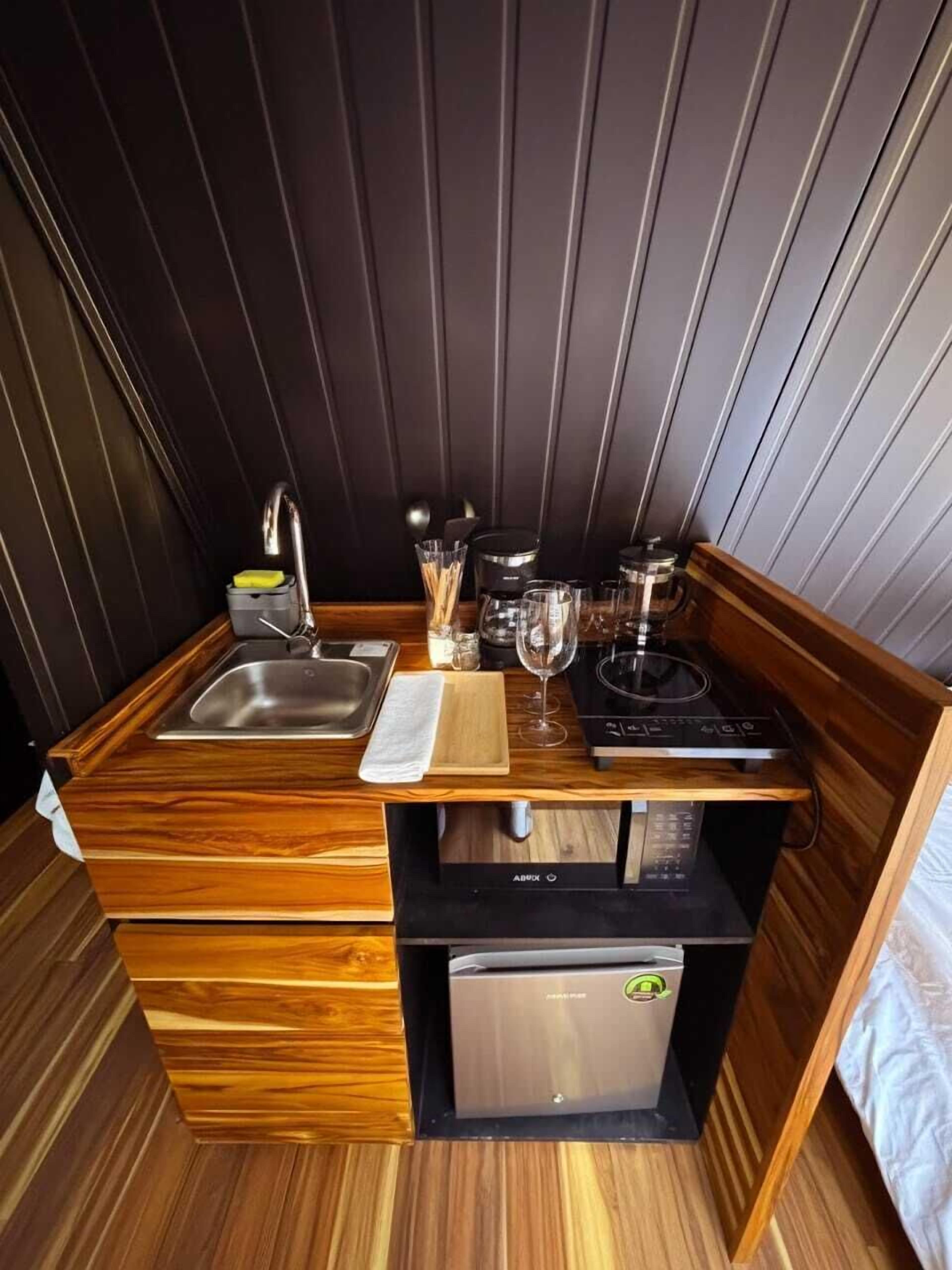 A compact kitchenette with a sink, a coffee maker, a wine glass, and a small refrigerator.