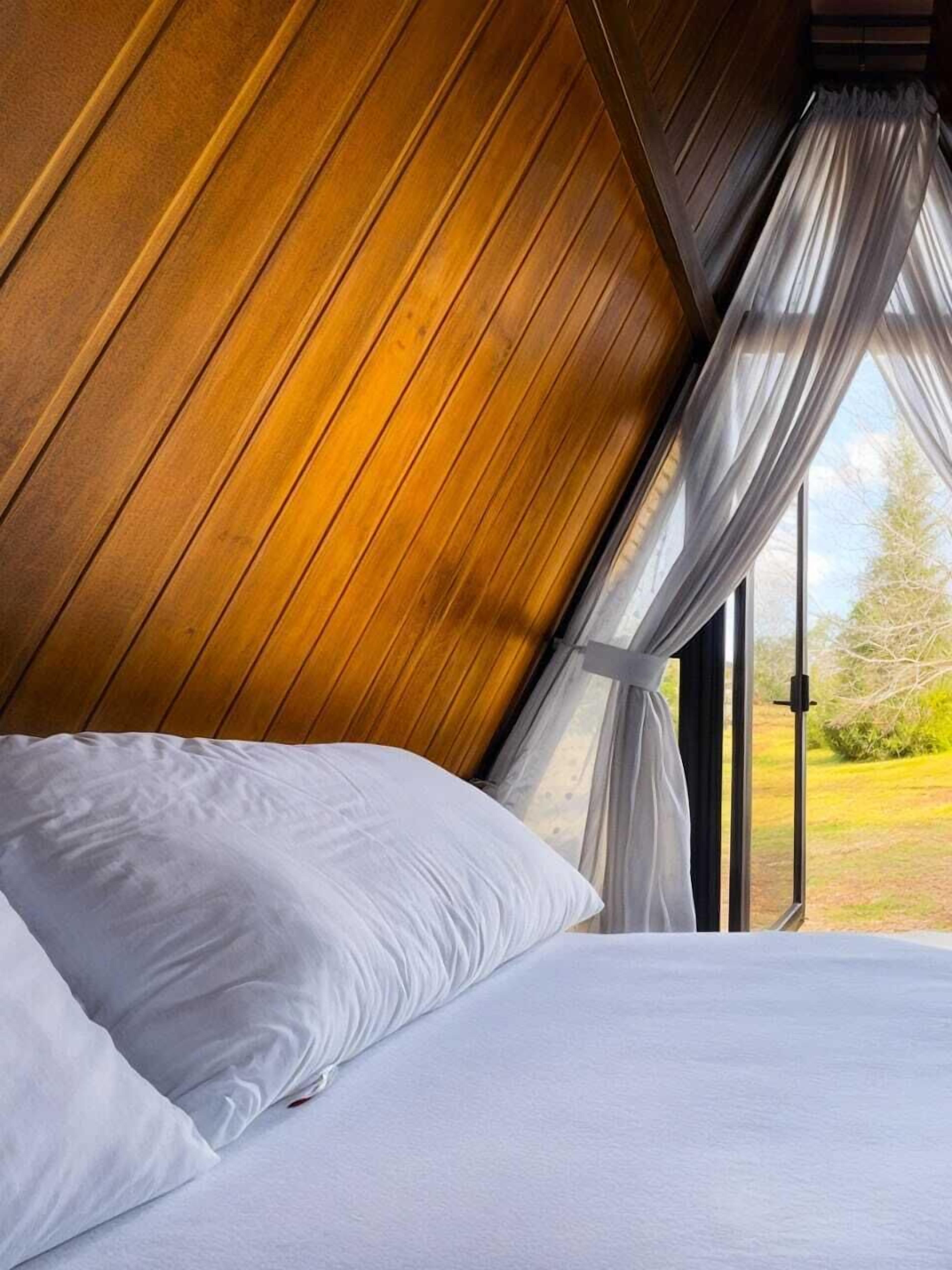 A bedroom with a sloped ceiling, a bed with white linens, and sheer curtains on a window.