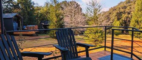 A wooden deck with two Adirondack chairs and a round table, overlooking a forested area.