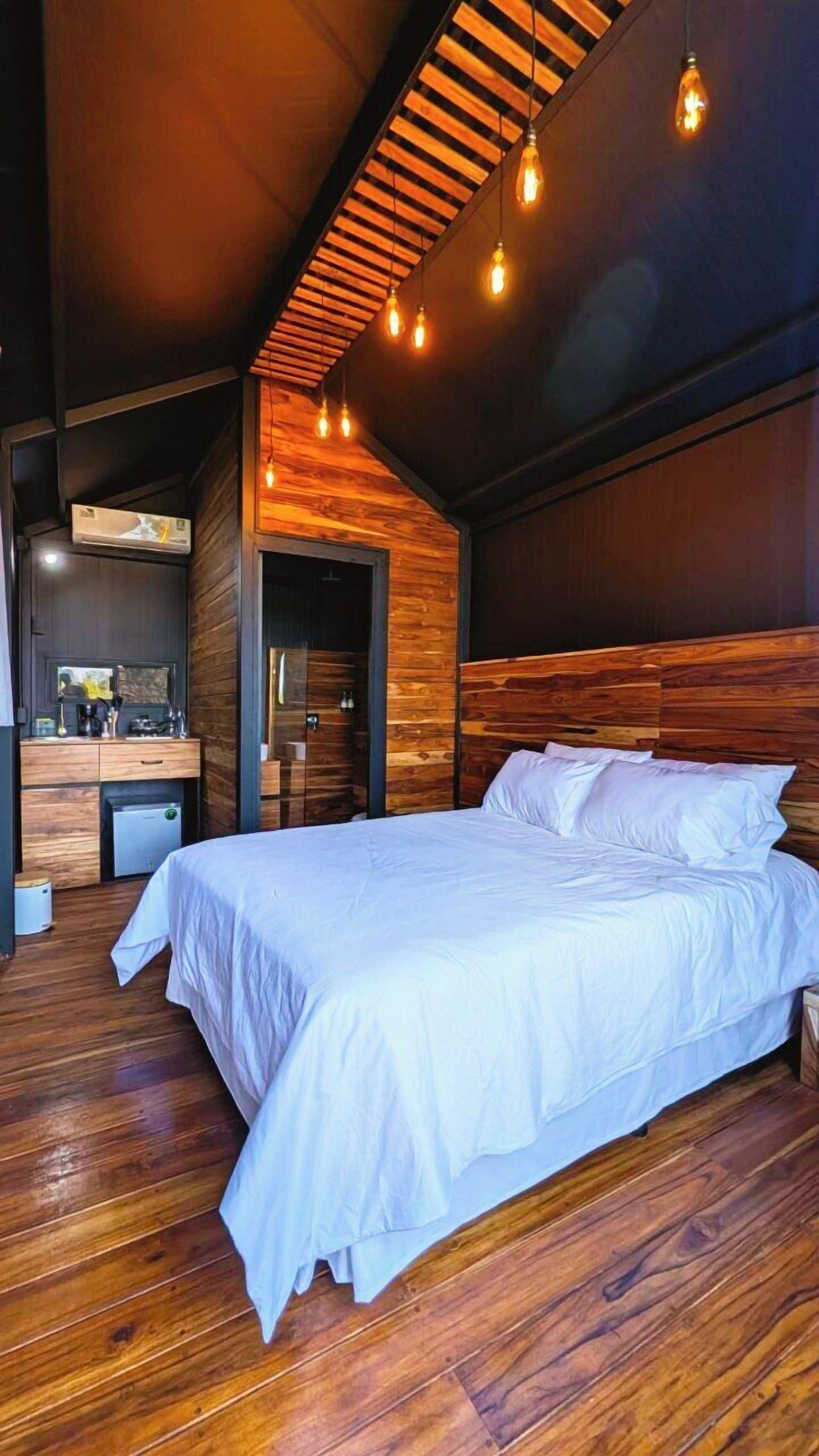 Une chambre avec un plafond en bois, un lit avec une literie blanche et un petit coin bureau.