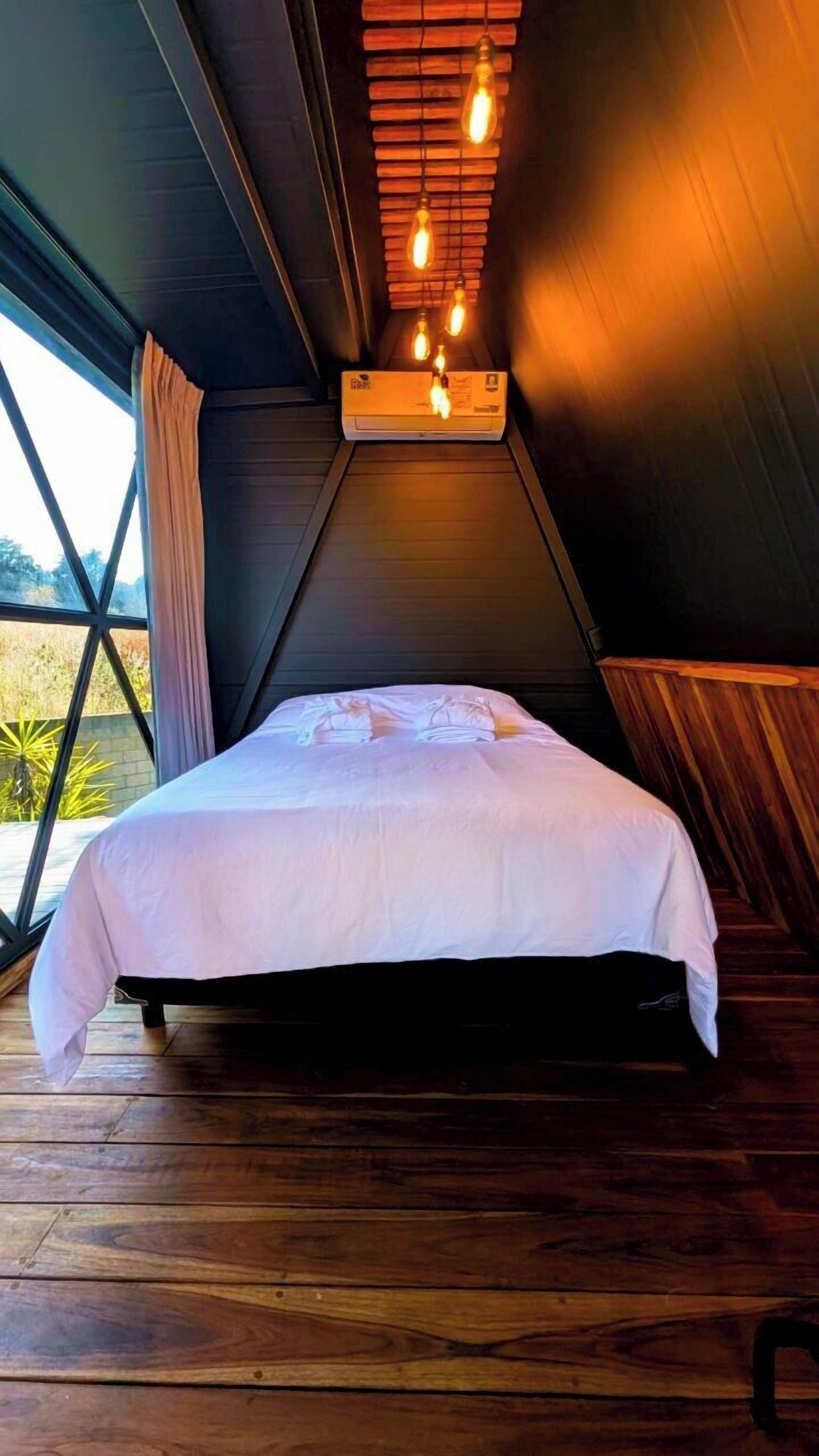 Un dormitorio con cama, suelo de madera y techo inclinado con luces colgantes.