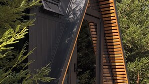 A modern, triangular wooden structure with a dark exterior and a wooden ramp leading to a door.