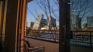Blick von einem Balkon mit Korbstuhl, Geländer und einer Skyline mit modernen Gebäuden.