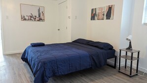 A bedroom with a large bed, a bedside table with a lamp, and a door. - Charming 1-bedroom apartment in welcoming Pittsburgh with AC (Pittsburgh)