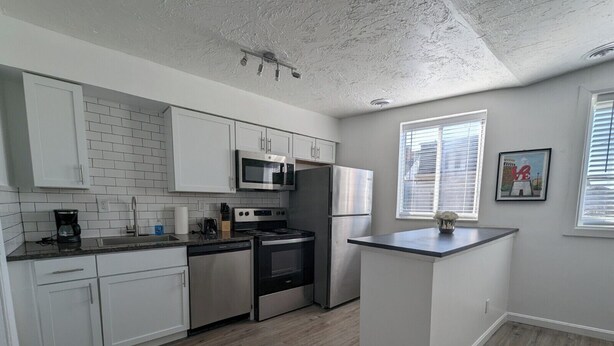 A modern kitchen with white cabinets, a stainless steel refrigerator, a microwave, and an oven. - Charming 1-bedroom apartment in welcoming Pittsburgh with AC (Pittsburgh)