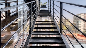 A modern staircase with metal railings, leading to an outdoor area with a view of surrounding buildings. - Rooftop - in Roma Norte (Mexico City)