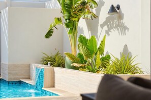 Un área de piscina con una pequeña cascada, rodeada de diversas plantas tropicales.
