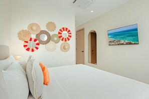 Habitación de hotel con cama, pared decorada con espejos y un cuadro de paisaje costero.