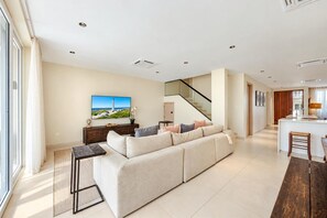 A spacious living area with a sofa, a flat-screen TV, and a staircase leading to an upper floor.