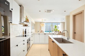 A modern kitchen with white cabinetry, a central island, and a view of a swimming pool. - Luxury 4BR Villa | Private Pool | Steps to Beach | Costa Catalina 1 by Bocobay (Noord)