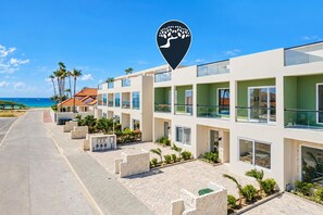 A beachfront hotel with multiple-story buildings, a paved walkway, and a clear view of the ocean. - Luxury 4BR Villa | Private Pool | Steps to Beach | Costa Catalina 1 by Bocobay (Noord)
