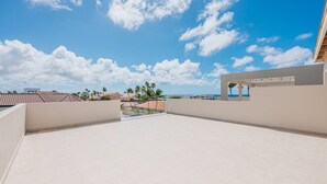 Eine Dachterrasse mit freiem Blick auf das Meer und Palmen.