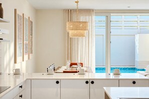 Cocina moderna con comedor, un amplio ventanal con vista a una piscina y una lámpara colgante.
