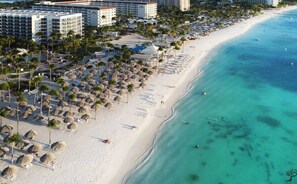 Un complejo turístico en la playa con varios edificios de hotel, palmeras y una playa de arena.