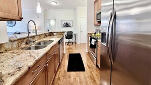 Une cuisine moderne dotée de plans de travail en granit, d’appareils électroménagers en acier inoxydable, d’armoires en bois et d’un tapis noir.