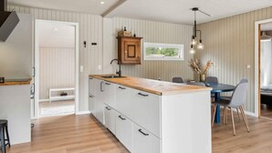 A modern kitchen with a central island, wooden flooring, and a dining area with a table and chairs. - 5 Star Holiday Home in Hals (Hals)