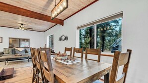 Un comedor con mesa y sillas de madera, un ventilador de techo y un ventanal con vistas a árboles.