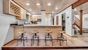 Una cocina moderna con armarios de madera, una isla central con taburetes y techo de madera.
