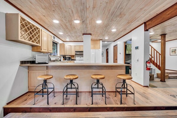 A modern kitchen with wooden cabinets, a central island with stools, and a wooden ceiling.