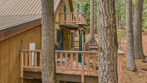 Una cabaña de madera con balcón y terraza, rodeada de árboles.