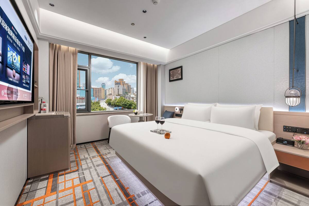 Ein Hotelzimmer mit einem großen Bett, einem Schreibtisch, einem Fernseher und einem Fenster mit Blick auf die Stadt.