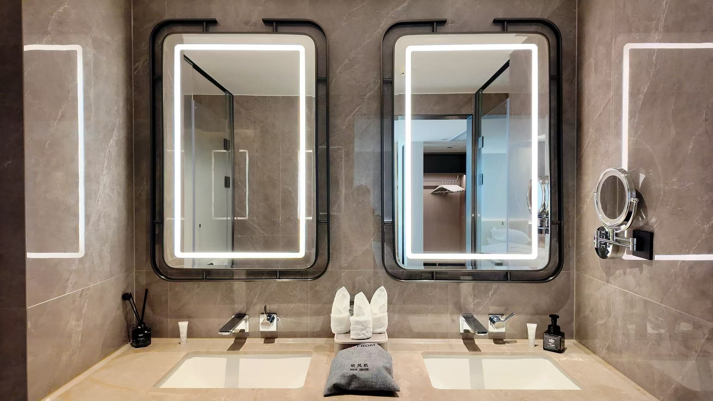 A modern bathroom with two sinks, a hair dryer, and a mirror with a light.