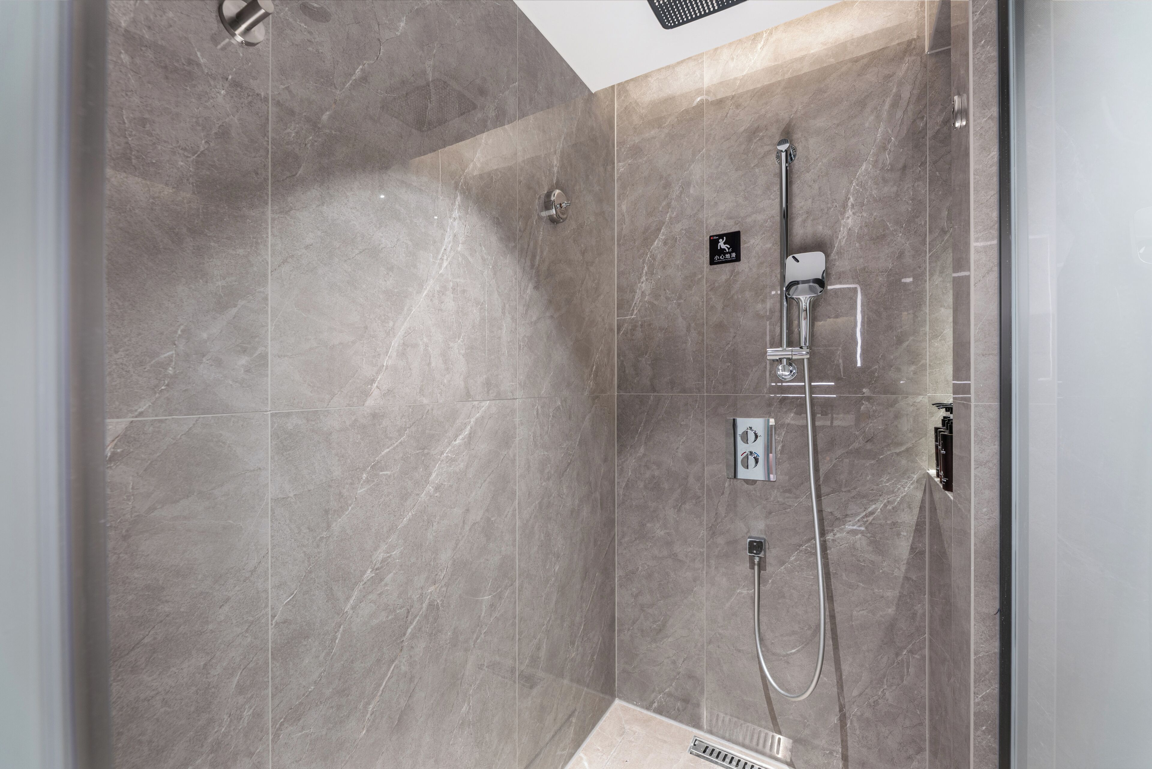 A modern shower with a handheld showerhead and a wall-mounted faucet, set in a room with large, smooth tiles.
