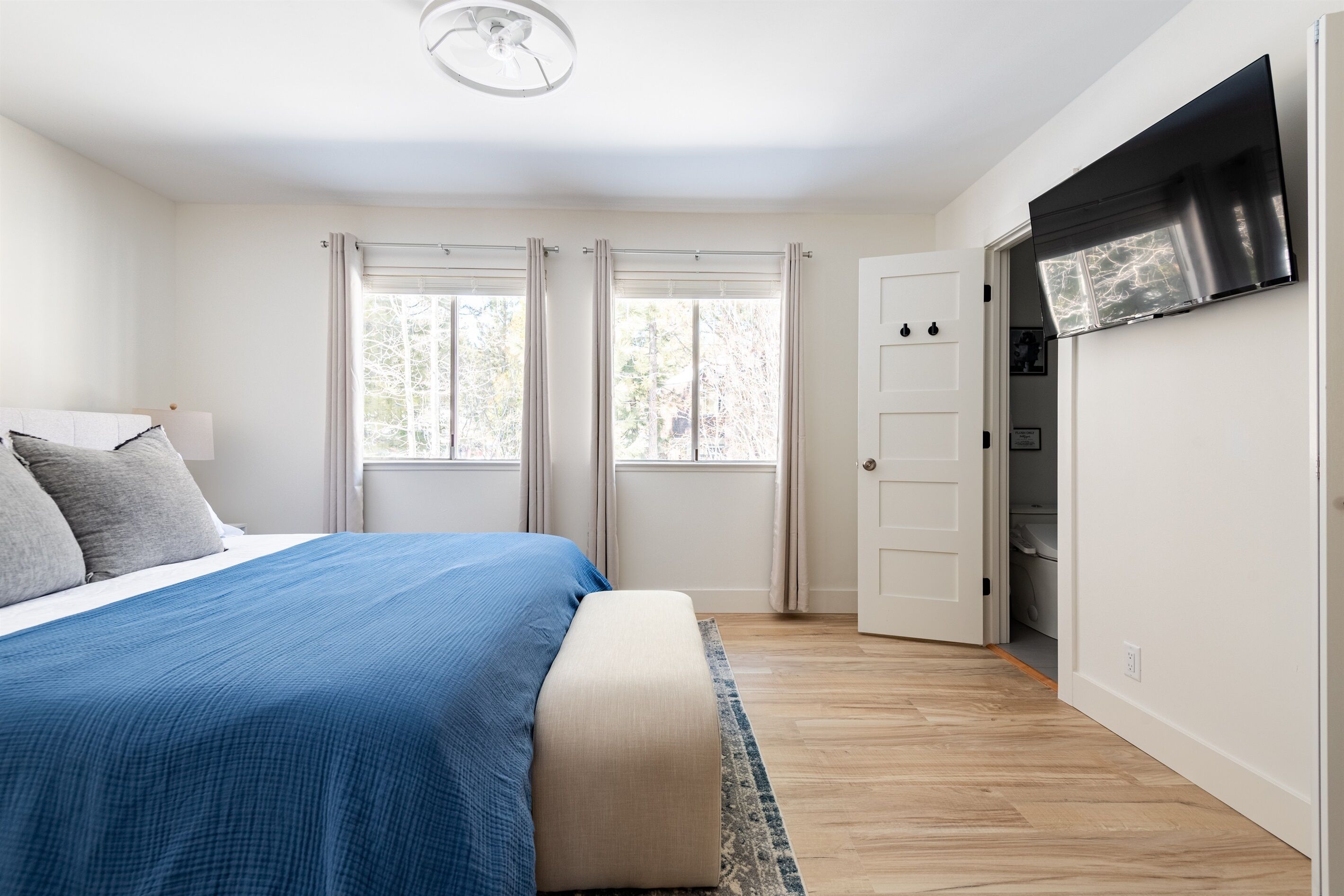 Een slaapkamer met een bed, twee ramen, een kledingkast en een plafondventilator.