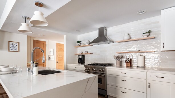A modern kitchen with a large island, white cabinetry, and stainless steel appliances.