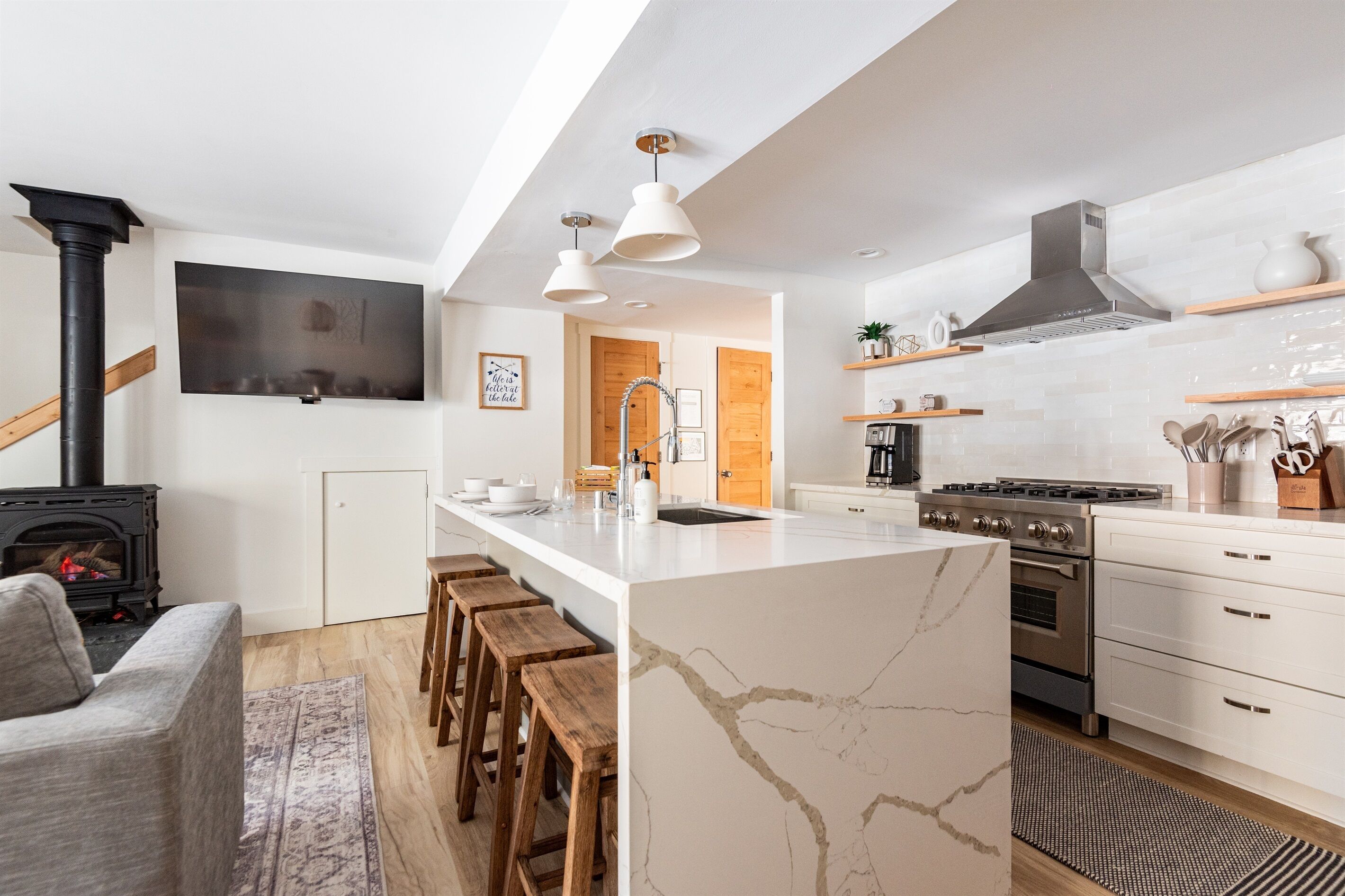Une cuisine moderne dotée d’un îlot central, de tabourets en bois, d’une cuisinière encastrée et de meubles de rangement blancs.