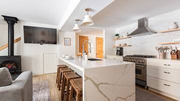 Une cuisine moderne dotée d’un îlot central, de tabourets en bois, d’une cuisinière encastrée et de meubles de rangement blancs.